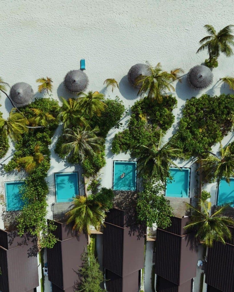 Vue aérienne verticale de villas tropicales avec piscines privées face à une plage de sable blanc
